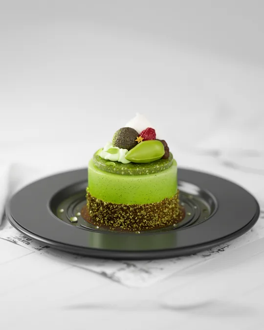 Studio-lit 3D render of a pistachio mousse dessert on a dark plate. Maya modeling, V-Ray lighting, Photoshop retouch.